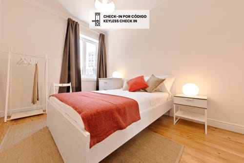 Modern bedroom with white bed, red bedding, and city view in Porto apartment with keyless check-in