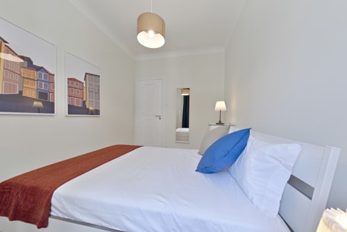 Modern bedroom in Porto apartment with white bedding, blue pillow, and city view artworks