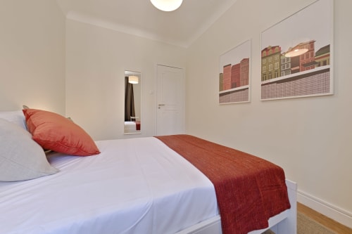 Modern Porto apartment bedroom with white linens, red accents, and city building artwork on wall