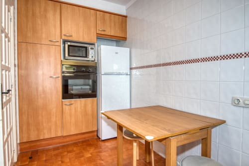 Cuina de fusta amb taula de menjador, frigorífic blanc i parets enrajolades a Finques Garcia Enrich, Palafrugell