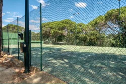 Pista de tennis de l'hotel Finques Garcia Enrich a Palafrugell envoltada d'arbres verds i cel blau