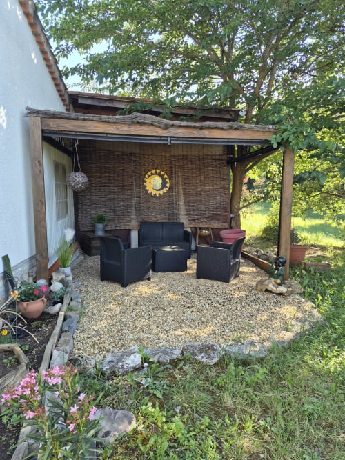 Área de descanso sombreada en Domaine en Terre Happy con muebles de ratán negro, biombo de privacidad tejido y jardín con flores