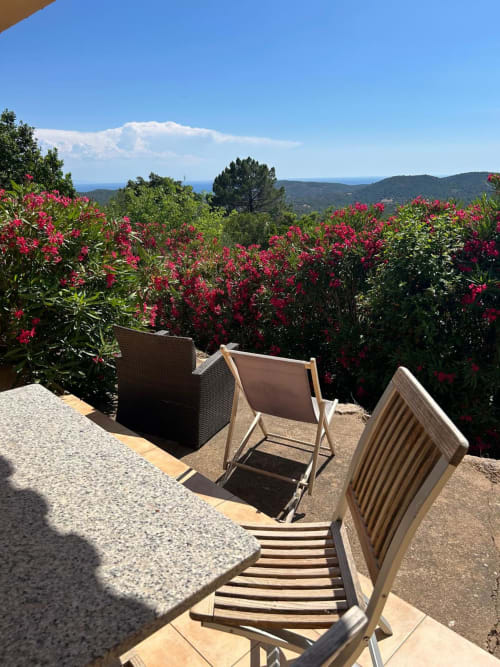 Terrasse Vista D'oro avec transats face aux fleurs rouges, collines forestières et vue sur la mer Méditerranée à Monacia d'Aullène