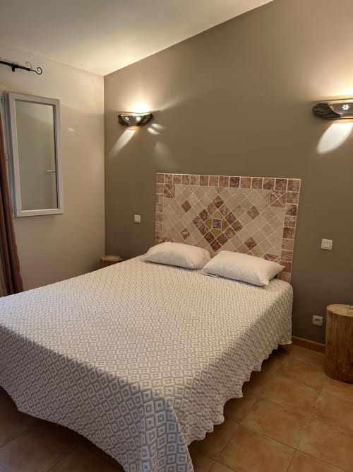 Chambre moderne de l'hôtel Vista D'oro à Monacia d'Aullène avec lit queen-size, tête de lit carrelée et éclairage chaleureux