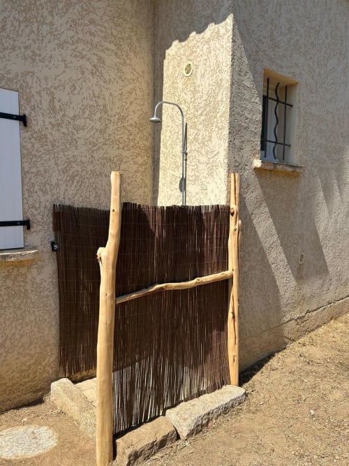 Douche extérieure rustique aux lames de bois à Vista D'oro à Monacia d'Aullène, Corse, avec murs en pierre traditionnels