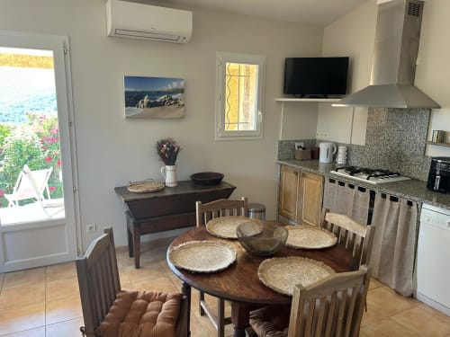 La chambre L'Alba à Vista D'oro avec table à manger, cuisine équipée, vue mer par la porte et décor côtier à Monacia