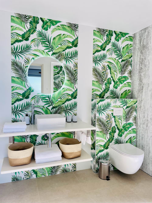 Salle de bain moderne avec papier peint tropical, vasque blanche, miroir éclairé, paniers tressés et toilettes murales
