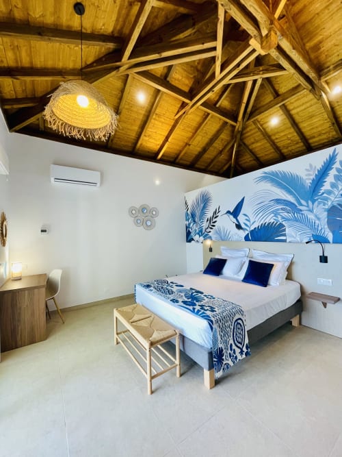 Chambre de villa face mer moderne avec œuvre d'art tropical bleu, plafond bois, literie blanche et vue sur mer au Marin