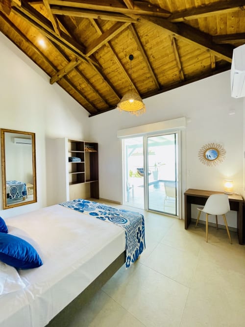 Chambre lumineuse à la Villa Nid des Colibris avec poutres apparentes, lin blanc, touches de bleu, bureau et vue sur mer