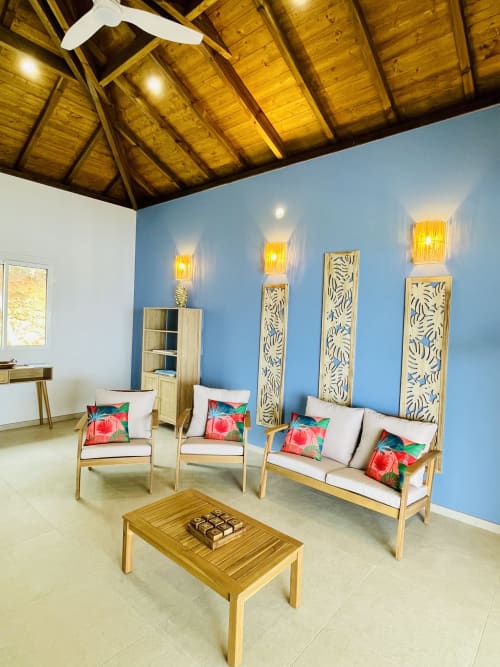 Salon de villa moderne aux murs bleus, plafond en bois, coussins floraux colorés sur mobilier clair et décoration murale