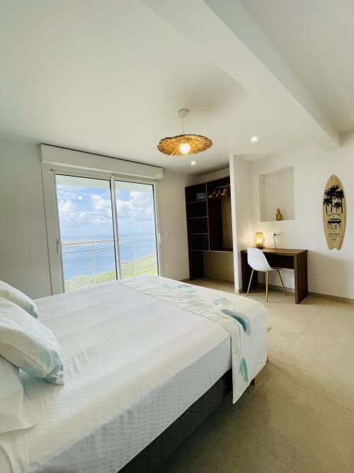 Chambre moderne à la villa Terrasses du Morne Gommier avec vue mer, lit blanc, bureau et balcon face à l'océan au Marin
