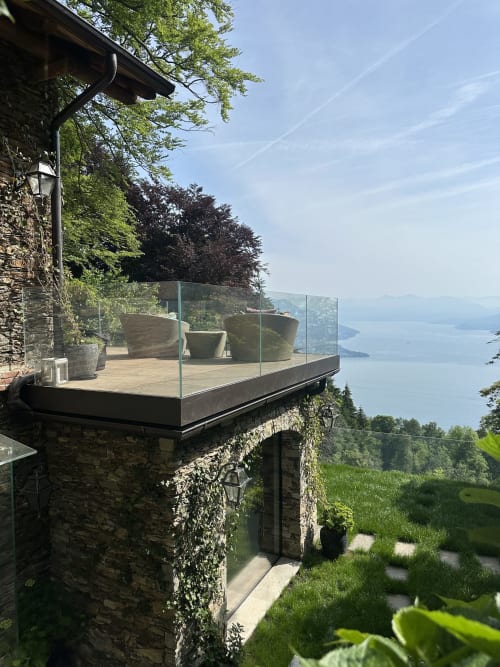 Luxuriöse Spa-Terrasse mit Glasgeländer über dem Lago Maggiore, Steinarchitektur, Blumenkübel, klarer Himmel