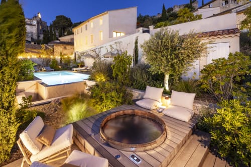 La cour de la Maison des Jardins au crépuscule avec foyer, piscine, transats et bâtiments blancs illuminés à Gigondas