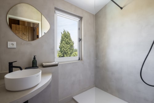 Salle de bain moderne à La Maison des Jardins avec vasque blanche, miroir rond et vue sur le jardin depuis la fenêtre à Gigondas