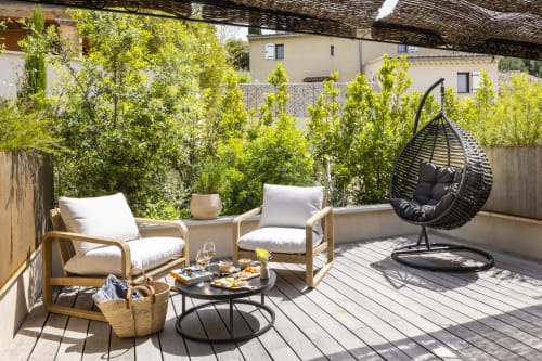 Terrasse ensoleillée aux jardins de La Maison des Jardins à Gigondas avec transats, balançoire et verdure luxuriante.
