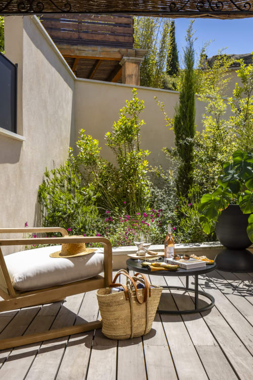 Terrasse ensoleillée à La Maison des Jardins avec transat en bois, table noire et vue sur le jardin luxuriant à Gigondas
