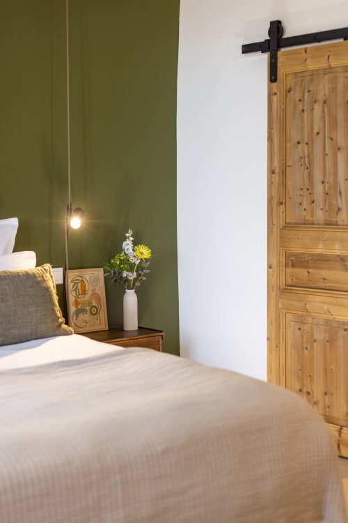 Chambre moderne à La Maison des Jardins B&B à Gigondas avec murs vert olive, porte grange en bois, fleurs fraiches et suspension