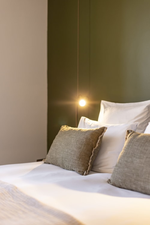 Chambre moderne de La Maison des Jardins Gigondas avec literie blanche, oreillers gris et éclairage d'ambiance chaleureux