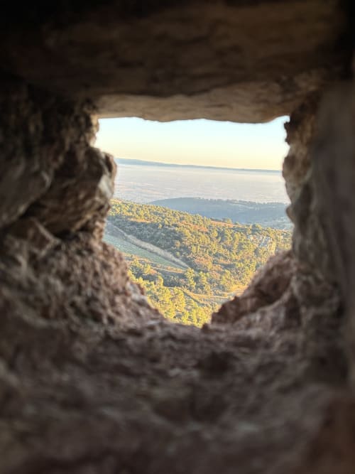 Encadrement de pierre offrant une vue sur la vallée de Gigondas, les collines boisées et un lac lointain à La Maison des Jardins