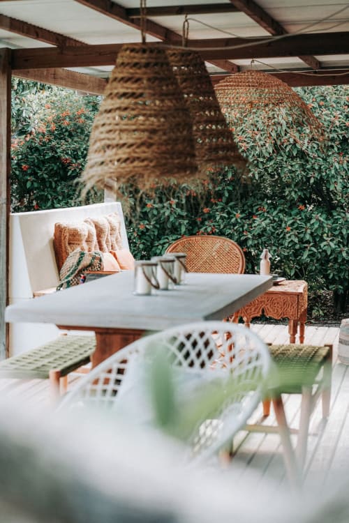 Patio de villa bord de mer à la Bleu Guesthouse avec luminaires suspendus tissés, mobilier blanc, fauteuils en rotin et vue luxuriante sur le jardin