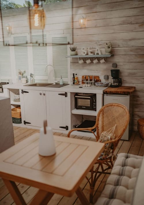 Kitchenette de la Suite Bleu Azur avec mobilier blanc, accents bois et chaise en rotin à la table à manger
