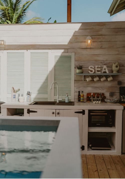 Cuisine extérieure à Bleu Guesthouse avec vue sur la piscine, équipée de meubles blancs, panneaux verts à jalousies, évier, cuisinière et bois