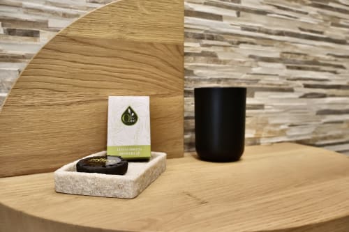 Esposizione di amenities luxury al Taga Rooms Catania: cuffia doccia alla citronella, candela nera e saponetta su tavolo in legno