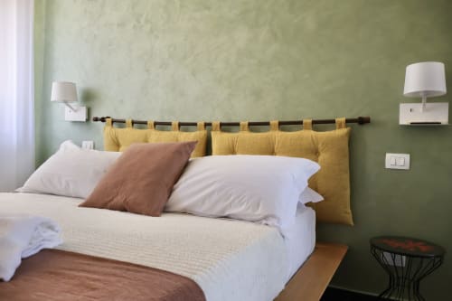 Camera moderna a Taga Rooms Catania con pareti verde salvia, cuscini gialli sulla testata, biancheria bianca e lampade notturne