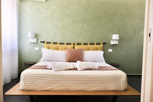 Camera moderna di Taga Rooms Catania con parete verde salvia, testata gialla, biancheria bianca e vista sulla città