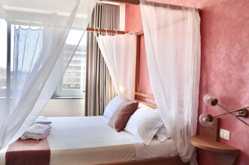 Lussuoso letto a baldacchino con veli bianchi trasparenti nella moderna camera d'hotel di Catania con pareti rosa e vista sulla città
