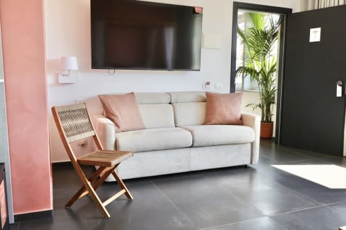 Elegante soggiorno presso Taga Rooms Catania con divano color crema, sedia in legno, TV a schermo piatto e pianta in vaso accanto alla porta nera