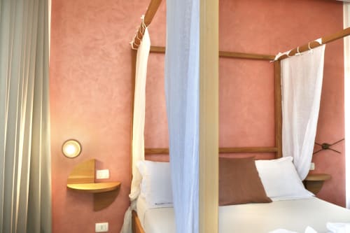 Letto a quattro colonne con baldacchino e biancheria bianca nella camera superior di Taga Rooms, Catania, con pareti color corallo e struttura in legno