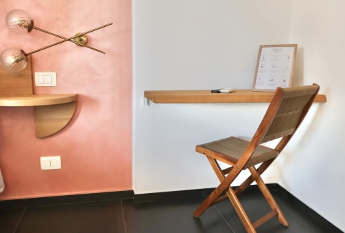 Stanza Superior di Taga Rooms Catania con area di lavoro con scrivania in legno, sedia mid-century, parete accent rosa e applique murale moderna