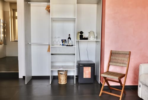 Camera moderna di Taga Rooms Catania con armadi integrati bianchi, minibar, macchinetta del caffè, sedia in legno e accenti rosa