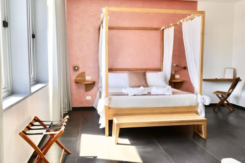 Spaziosa camera superior presso Taga Rooms Catania con letto a quattro colonne in legno, parete accent color corallo, tende bianche trasparenti e vista città