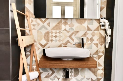 Lavabo moderno con bacinella bianca su piano in legno, piastrelle geometriche a rivestimento e scala portasciugamani presso Taga