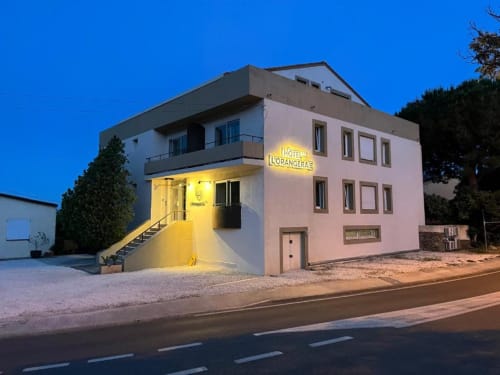 Hôtel l'Orangeraie at dusk in Le Lavandou, pink building with yellow entrance and illuminated signage