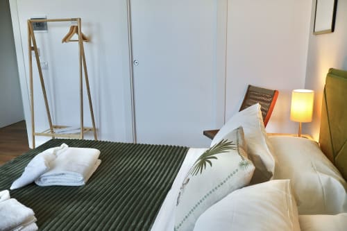 Camera moderna a Taga Rooms Catania con letto verde, cuscini bianchi, appendiabiti in legno e calorosa lampada da comodino