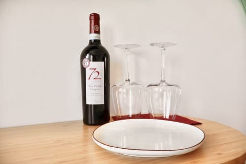 Bottiglia di vino rosso con bicchieri e piatto su tavolo in legno al boutique hotel Taga Rooms a Catania