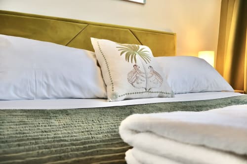 Elegante letto presso Taga Rooms Catania con testiera dorata, cuscini bianchi, cuscino decorativo botanico e tessuto verde texturizzato
