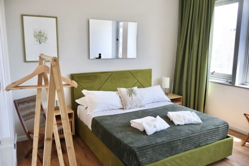 Camera moderna a Taga Rooms Catania con letto rivestito in verde, cuscini bianchi, appendiabiti in legno e vista sulla città