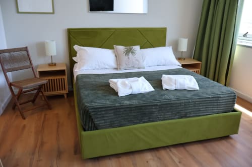 Spaziosa camera da letto a Taga Rooms Catania con letto rivestito verde oliva, cuscini bianchi, TV a schermo piatto e servizi moderni