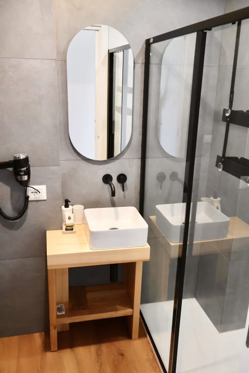 Bagno moderno alle Taga Rooms Catania con specchio ovale, lavabo bianco, vanità in legno e box doccia in vetro