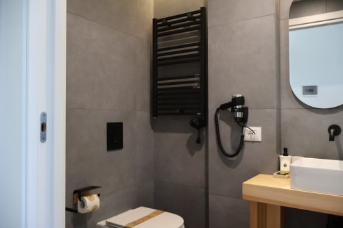 Moderno bagno di Taga Rooms a Catania con scaldasalviette nero, lavabo bianco, specchio rotondo e wc