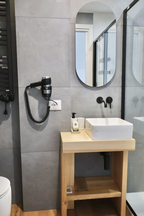 Bagno moderno di Taga Rooms Catania con specchio ovale, mobile lavabo in legno, rubinetteria nera e pareti rivestite in piastrelle grigie