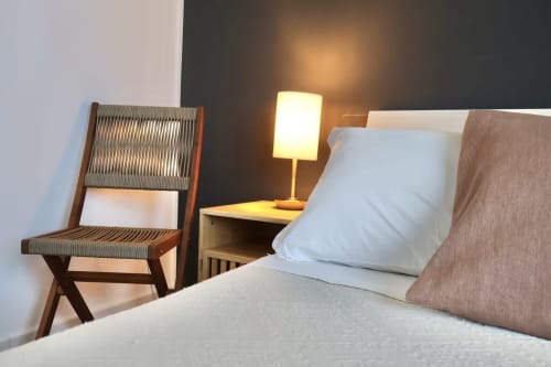 Camera moderna di Taga Rooms Catania con letto, sedia in legno, lampada da comodino e parete scura in contrasto