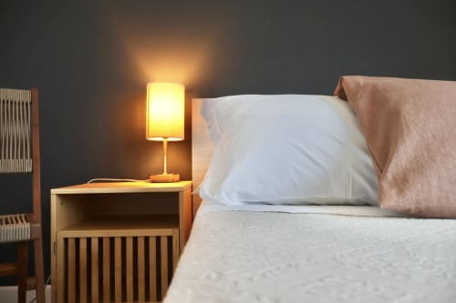 Camera accogliente a Taga Rooms Catania con lampada comodino illuminata, cuscino bianco, comodino in legno e vista sulla città