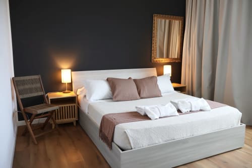 Camera moderna a Taga Rooms di Catania con letto bianco, accenti marrone, comodini, specchio, poltrona e vista sulla città