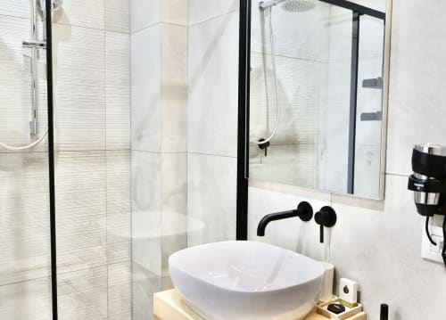 Bagno moderno presso Taga Rooms Catania con lavabo bianco, rubinetteria nera e soffione a pioggia dietro divisorio in vetro