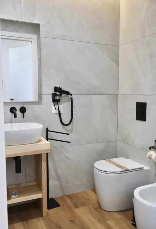 Bagno moderno a Taga Rooms Catania con piastrelle in marmo, lavabo bianco e finiture nere